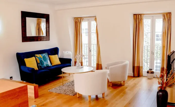 Shared lounge with blue sofa, armchairs and tall windows at PROMIS Kendrick Mews
